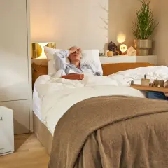 Hombre cuida a mujer enferma en cama. Purificador de aire Daikin al lado, mejorando la calidad del aire iaq.