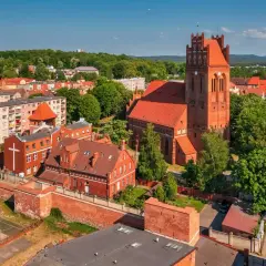 Zamek krzyżacki w Lęborku, z charakterystyczną wieżą i ceglaną architekturą, otoczony zielenią i miejską zabudową.