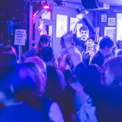 Ambiance festive dans un bar du Marais, une foule profite de la musique sous des lumières bleues et violettes.