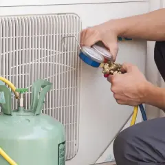 Técnico revisa manómetro para detectar fuga aire acondicionado. Cilindro de gas refrigerante y unidad exterior visibles.