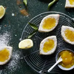 Italienische Kekse mit Lemon Curd, bestäubt mit Puderzucker, auf einem Gitter und dunklem Untergrund.