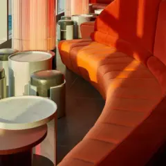 Arredamento moderno con divano curvo arancione e sgabelli in un w barcelona rooftop bar con vista sul mare.