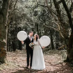 Szczęśliwa para podczas sesji ślubnej w lesie, trzymająca balony z napisami "Mr" i "Mrs".