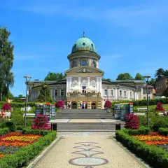 Piękny budynek uzdrowiskowy z kopułą, otoczony kwitnącym ogrodem i alejkami. Idealne miejsce na relaks i spacer, jakby czas się tu zatrzymał.