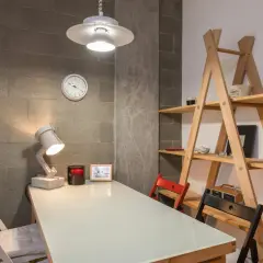 Stół z krzesłami i lampką, obok regał. Jak wyciszyć mieszkanie w bloku? Ceglana ściana i drewniane elementy tworzą przytulny klimat.