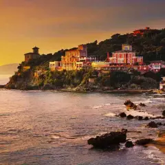 Ville colorate aggrappate alla scogliera, con il mare che lambisce la costa rocciosa. Un tramonto dorato illumina i borghi vicino Castiglioncello.