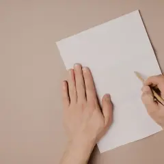 Ręce piszą list motywacyjny po angielsku na białej kartce.