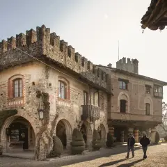 Antico borgo Visconti a Piacenza, con torri merlate e archi in pietra. Due uomini passeggiano nel cortile illuminato dal sole.