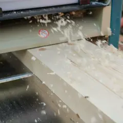 Le bois est raboté avec précision par la dégau rabot, créant une surface lisse et des copeaux fins qui volent dans l'air.