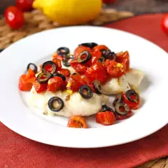Delizioso merluzzo in friggitrice ad aria, condito con pomodorini e olive nere, pronto per essere gustato.