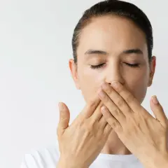 Donna con occhi chiusi copre la bocca con le mani, un'espressione di **bocca amara** sul volto.