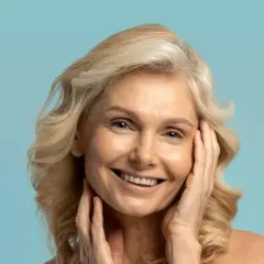 Uśmiechnięta kobieta z blond włosami, której skóra lśni dzięki olejkowi kameliowemu.
