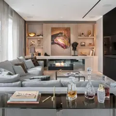 Nowoczesny salon w stylu nowojorskim. Szara kanapa, kominek, dzieło sztuki i eleganckie dekoracje tworzą przytulną atmosferę.