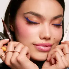 Mujer con delineado azul vibrante y varios eyeliners de colores en sus manos. Descubre qué es el eyeliner perfecto para ti.