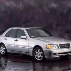 Srebrny Mercedes-Benz C-Klasa W202 z lat 90. na tle ciemnego, malowanego tła.