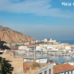 Widok na portowe miasto Oran, z górami w tle i licznymi łodziami na wodzie.