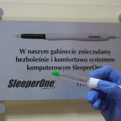Ręka w niebieskiej rękawiczce trzyma komputerowy system znieczulający SleeperOne. Dowiedz się, ile trzyma znieczulenie u dentysty.