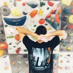 Wspinaczka bouldering na kolorowej ściance. Mężczyzna z rękami za głową, przygotowuje się do pokonania trudnej trasy.