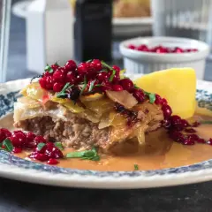 En portion kålpudding med lingon och en potatisklyfta. Ett klassiskt svenskt recept som är perfekt för en mysig middag.