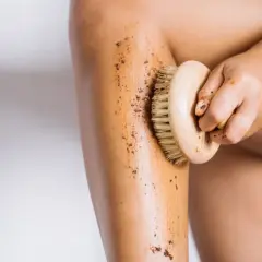 En hand använder en borste för att exfoliera benet med en brun skrubb. Det är ett bra sätt att få mjuk hud.