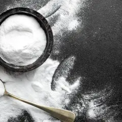 Biały proszek, prawdopodobnie soda oczyszczona na mrówki, w miseczce i na łyżce na czarnym tle.