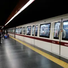 Des voyageurs attendent sur le quai du **metro a Rome**. Un train blanc et bordeaux arrive, reflétant les lumières du tunnel.