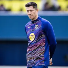 Robert Lewandowski w stroju FC Barcelona, w tle niebieska ściana. Wokół niego krążą barcelona pogłoski transferowe.