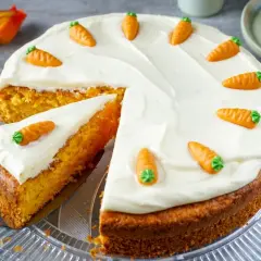 Saftiger Karottenkuchen mit cremiger Glasur und kleinen Marzipan-Karotten. Ein Stück ist bereits angeschnitten.