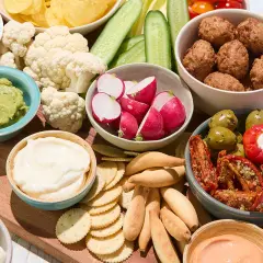 Un plateau garni pour un apéro d'été : boulettes, crudités, guacamole, fromages, olives et tomates séchées.