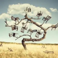 Drzewo pełne krzeseł, jakby wyrosło z nich, tworząc surrealistyczne omamy. Na trawiastym polu leżą połamane meble.