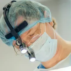 Kirurg med lupp och mask utför buccal fat removal i Sverige.