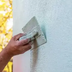 Ręka fachowca wygładza świeży tynk gąbką. Gąbkowanie tynku po jakim czasie daje najlepszy efekt?