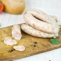 Gotowe jelita do kiełbasy leżą na desce, obok pomidora i przypraw.
