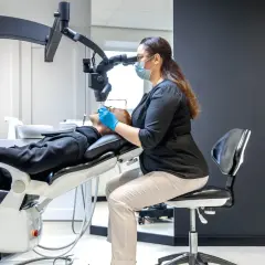 Dentystka pod mikroskopem bada ząb pacjenta. To moment, kiedy potrzebne jest leczenie kanałowe.