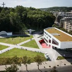 Nowoczesny budynek Gdyńskiego Centrum Filmowego z zielonym dachem, otoczony parkiem z amfiteatrem i krzyżem na wzgórzu.