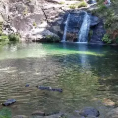Un hombre disfruta de las pozas de Mougas, con cascadas cayendo sobre rocas y agua cristalina.