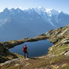 Widok na wejście na Mont Blanc. Turysta z plecakiem stoi nad górskim jeziorem, podziwiając ośnieżone szczyty.