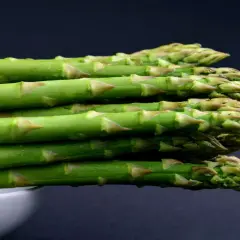 A stack of fresh green asparagus spears with water droplets, against a dark background.