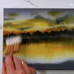 Peinture au scotch d'un paysage au coucher du soleil, avec des nuages orangés et jaunes reflétés dans l'eau.
