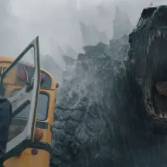 Enorm Godzilla vrålar mot en gul skolbuss i regnet, en del av **Monarch Legacy of Monsters**.