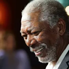 Uśmiechnięty aktor murzyn, Morgan Freeman, z siwą brodą i kręconymi włosami, w garniturze.