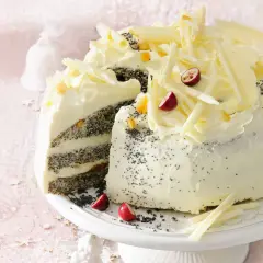 Pyszny tort makowy mojej mamy, udekorowany kremem, białymi czekoladowymi wiórkami, żurawiną i kandyzowaną skórką pomarańczową.
