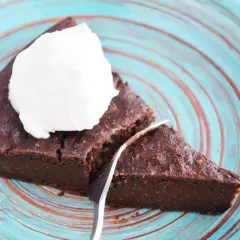 Pyszny brownie z cukinii codziennie fit, podane z bitą śmietaną na turkusowym talerzu.