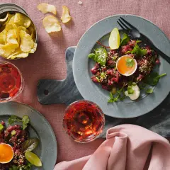Två tallrikar med asiatisk råbiff, toppad med äggula och sesamfrön. Serveras med potatischips och rosévinsglas.