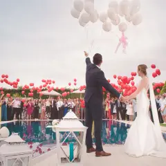 Mariés lançant des ballons rouges et blancs lors d'une animation mariage, avec des invités autour d'une piscine.