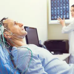 Pacjent leży z elektrodami na głowie podczas badania EEG. Czy badanie eeg czy boli? Nie, jest bezbolesne. Lekarka analizuje wyniki.