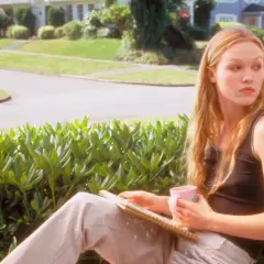 Kat Stratford, protagonista di "10 cose che odio di te trama", pensierosa con una tazza rosa e un quaderno.