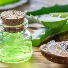 Ein Glas mit grünem Aloe Vera Gel und eine Holzschale mit Aloe Vera Stücken. Die vielseitige aloe vera verwendung für Haut und Gesundheit.