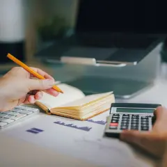 Un avocat postulant analyse des documents financiers avec un crayon, une calculatrice et un ordinateur portable.