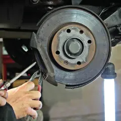 Mains d'un mécanicien utilisant des outils pour changer un disque de frein usé sur une voiture.